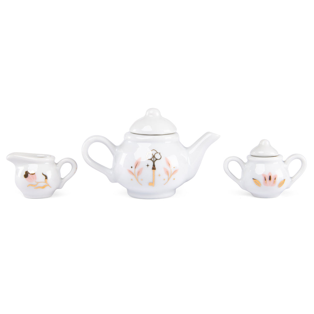 Three white ceramic teapot pieces featuring simple illustrations: a small pitcher, a medium teapot with a floral design, and a tiny sugar bowl.