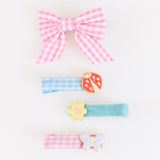 Four hair clips: a pink gingham bow, a ladybug on blue gingham, a yellow flower, and a lavender butterfly.