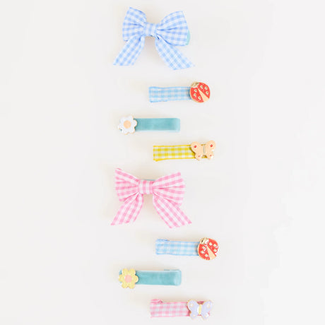 A vertical row of colorful gingham bows and fabric hair clips featuring ladybug, flower, and butterfly charms.