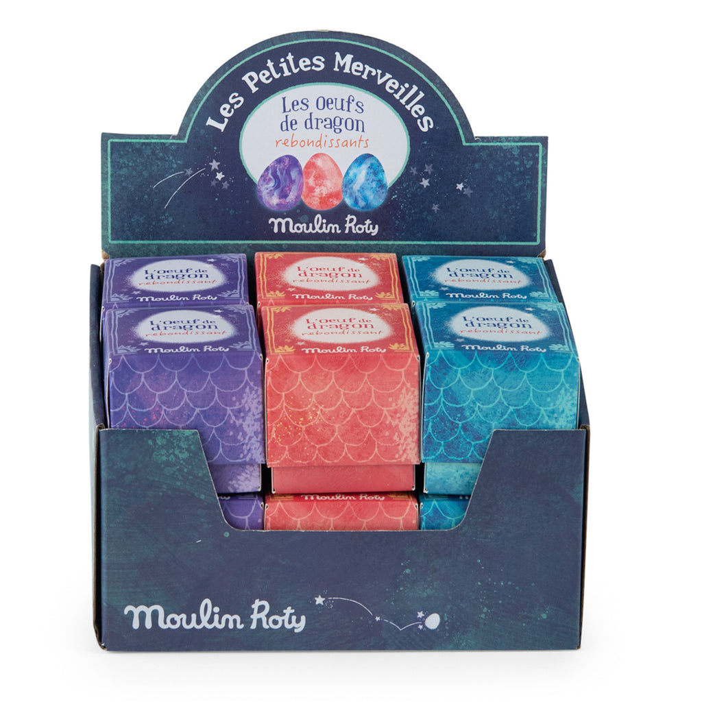 Display box of colorful "Moulin Roty Les Petites Merveilles" dragon eggs. Packaging features purple, red, and blue scaled designs, conveying a magical theme.