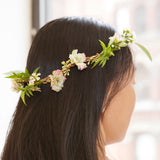 Rear view of a person with long dark hair wearing a delicate crown of fresh white and pink flowers with green leaves.