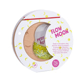 A Petit Boum Flow Moon sensory toy in its original packaging, featuring a crescent-shaped wooden frame filled with yellow glitter and glow-in-the-dark elements.