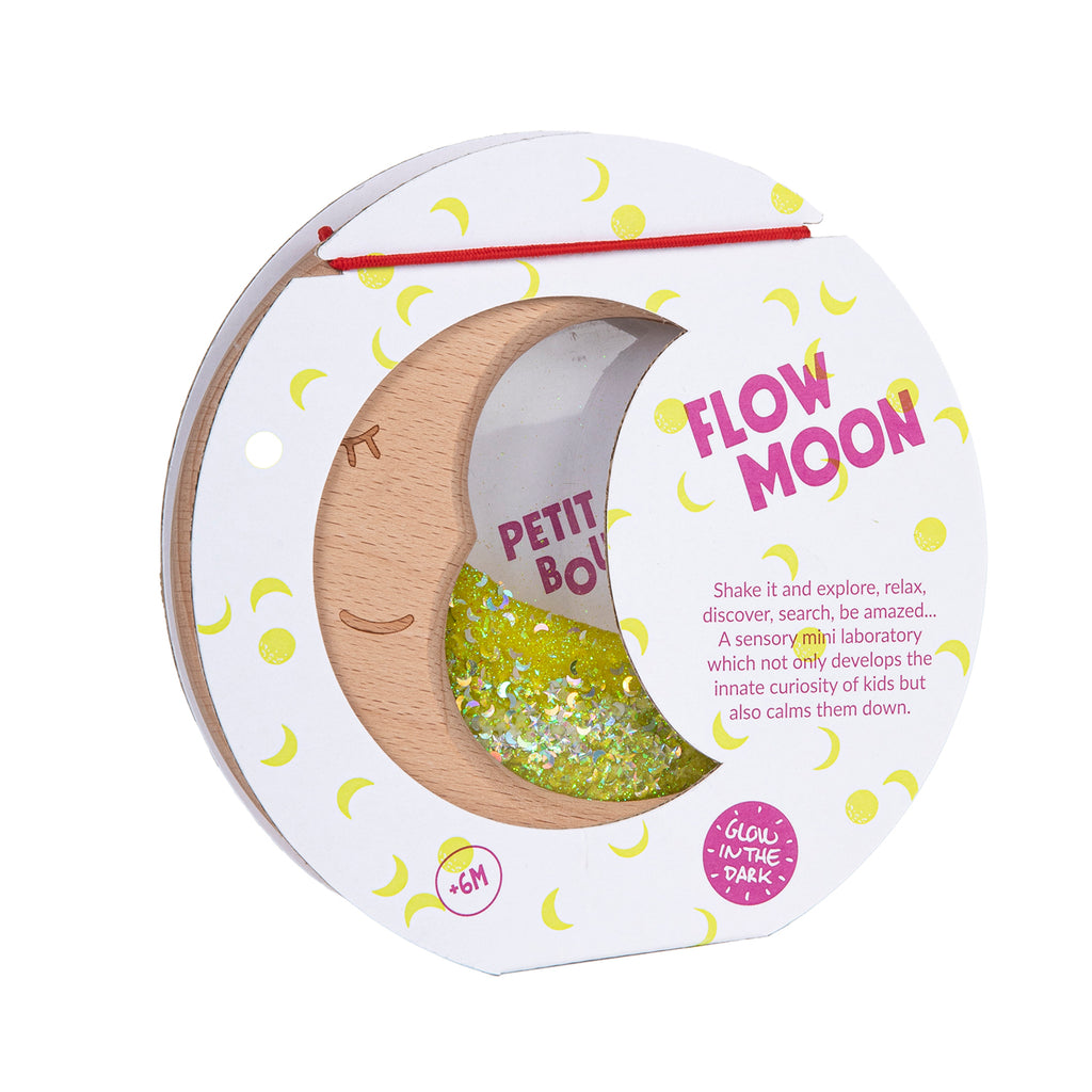 A Petit Boum Flow Moon sensory toy in its original packaging, featuring a crescent-shaped wooden frame filled with yellow glitter and glow-in-the-dark elements.