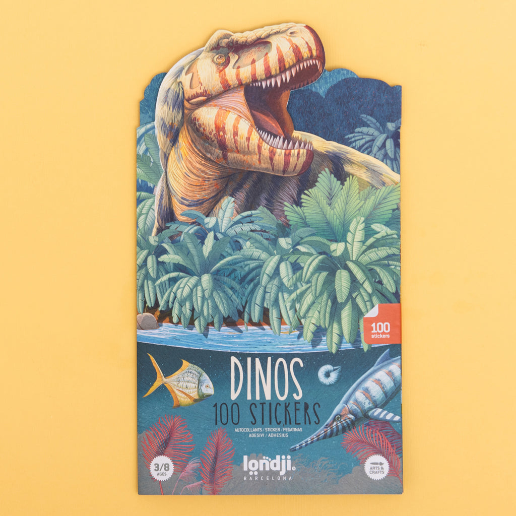 Sticker booklet with a colorful illustration of a roaring dinosaur amidst lush ferns and palms, set against a yellow background. Text reads, "Dinos 100 Stickers."