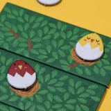 Londji Piu Piu board game features bird and egg tokens on green leaf-patterned tiles against a yellow background.