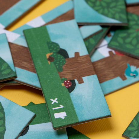 Close-up of Londji Piu Piu counting game tiles featuring colorful bird and tree illustrations on a yellow background.