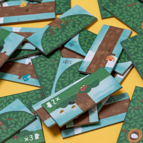 Scattered Londji Piu Piu board game tiles featuring illustrated trees, birds, and bees on a bright yellow background.