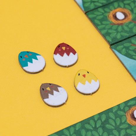Four colorful bird egg game pieces from Londji's Piu Piu game on a yellow background with green nesting tiles.