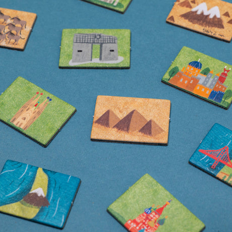 Close-up of illustrated landmark game tiles including the Pyramids, Sagrada Familia, and Golden Gate Bridge on blue.