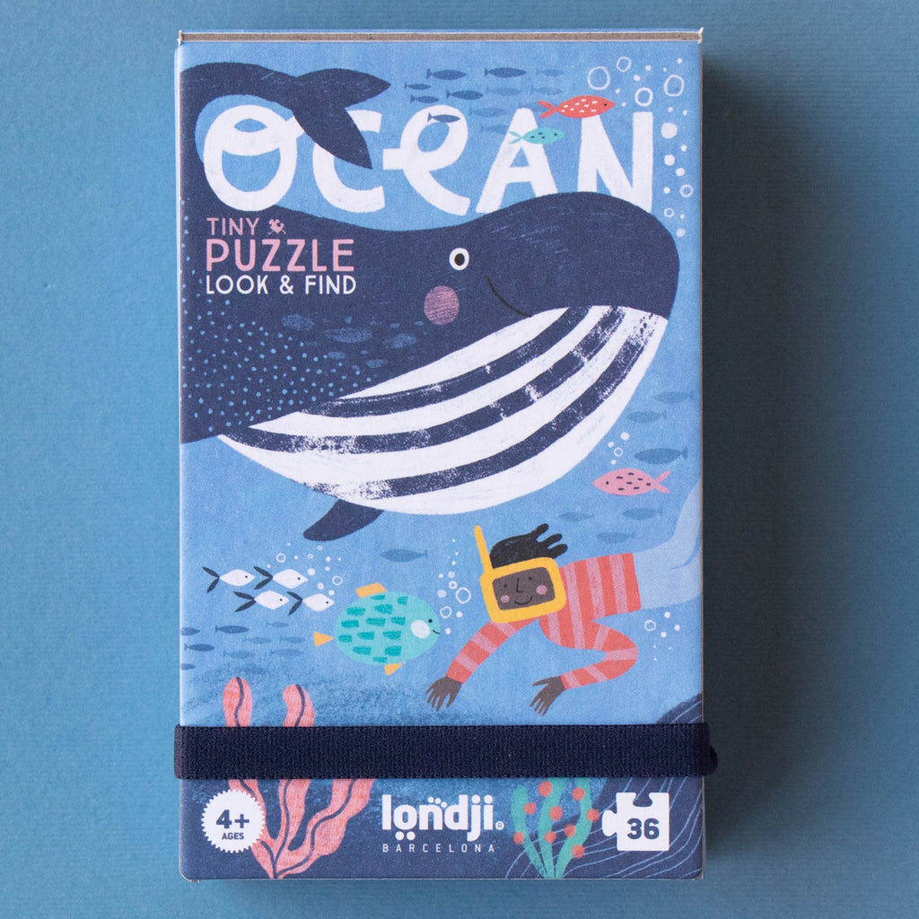 Illustrated puzzle box depicting a smiling whale, colorful fish, and a diver. Text reads "Ocean Tiny Puzzle Look & Find" for ages 4+. Vibrant sea theme.