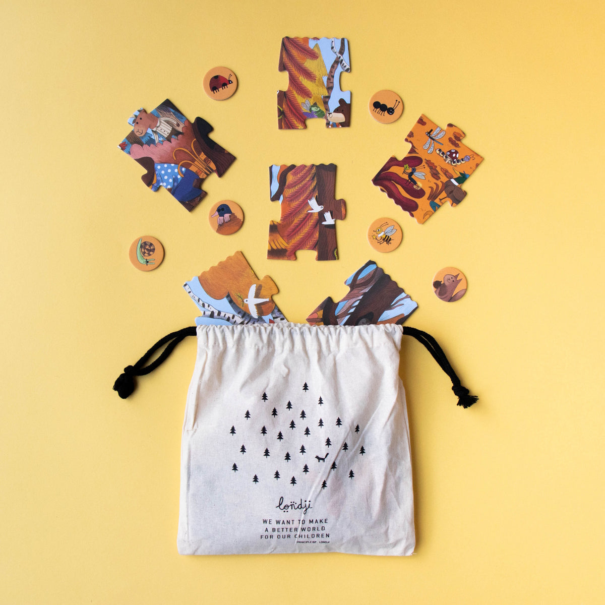 A flat lay of the Londji "We Want to Make a Better World" forest-themed memory game with jigsaw pieces and chips on yellow.