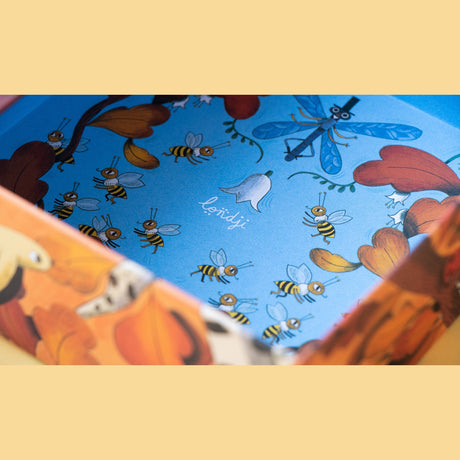 Londji puzzle box interior with whimsical illustrations of bees, a dragonfly in a top hat, and autumn leaves.