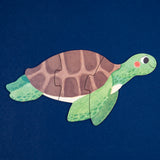 Sea turtle shaped Londji jigsaw puzzle for kids, featuring a green turtle with a brown shell on a navy blue background.