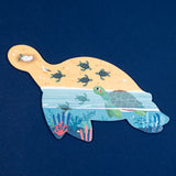 Sea turtle shaped Londji jigsaw puzzle featuring baby turtles on a beach and swimming in a coral reef illustration.