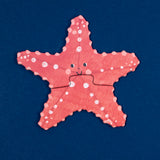 Smiling pink starfish Londji puzzle with white spots on a dark blue background.