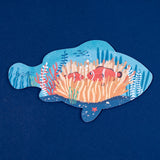 Fish-shaped jigsaw puzzle featuring an illustration of two clownfish in an orange anemone on a dark blue background.
