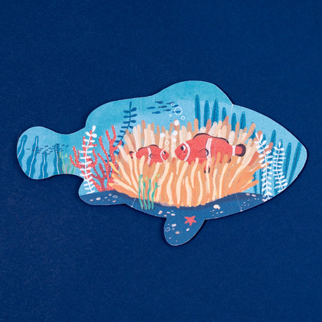 Fish-shaped jigsaw puzzle featuring an illustration of two clownfish in an orange anemone on a dark blue background.