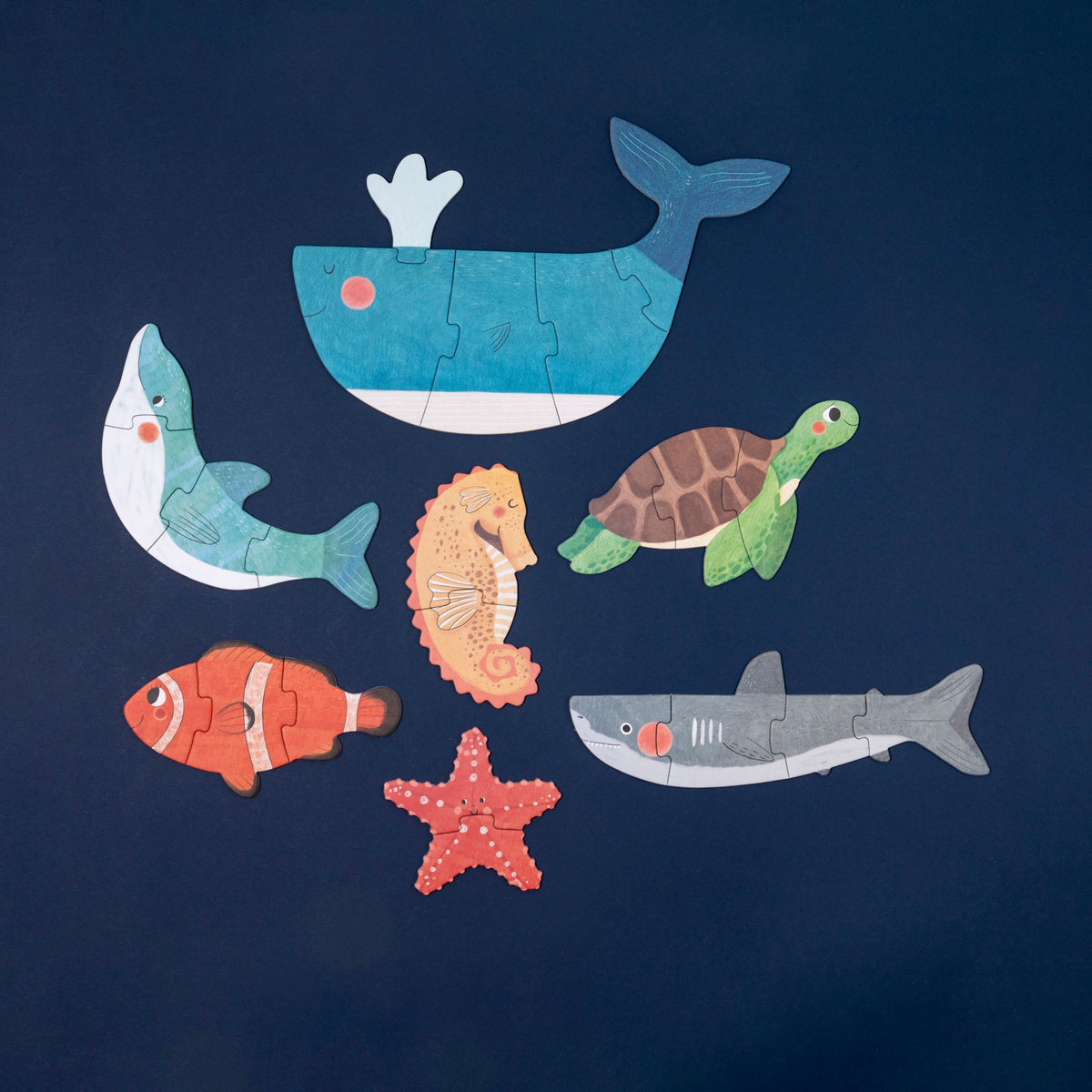 Seven colorful Londji wooden sea animal puzzles, including a whale, turtle, and shark, arranged on a dark blue background.