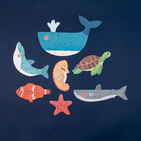 Seven colorful Londji wooden sea animal puzzles, including a whale, turtle, and shark, arranged on a dark blue background.