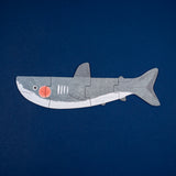 A Londji wooden shark puzzle featuring a grey shark with a red cheek, composed of four pieces on a dark blue background.