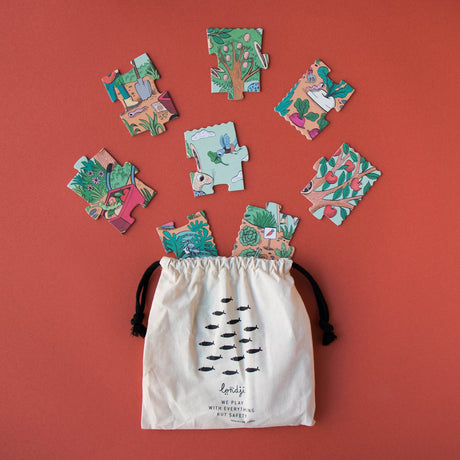 Londji Rabbit's Garden puzzle pieces scattered above a cream drawstring cotton bag on a terracotta background.