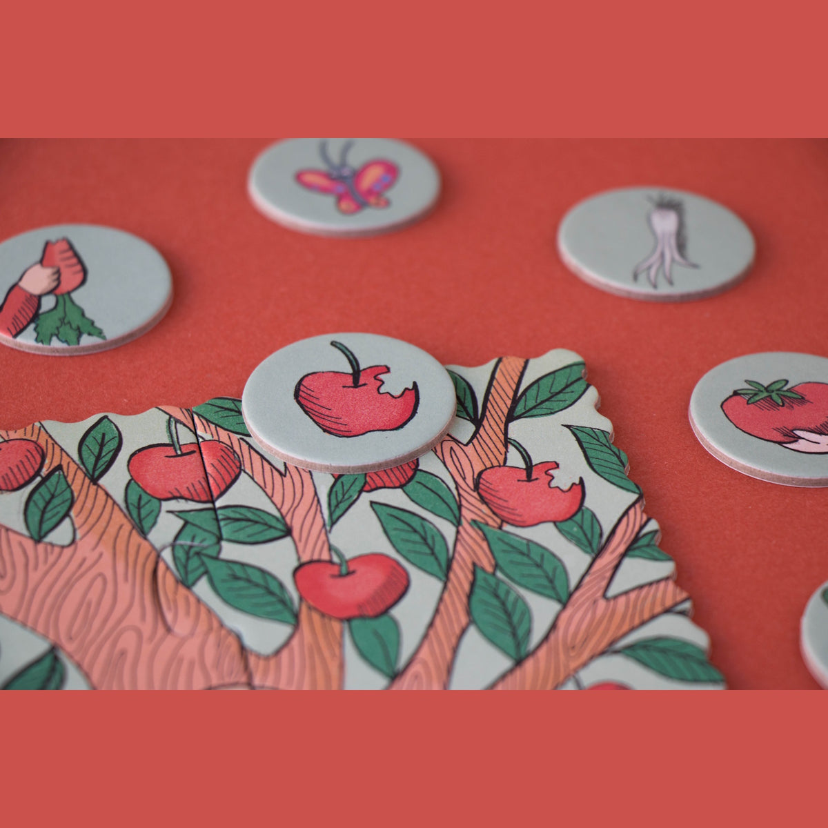 Close-up of a Londji puzzle piece showing an apple tree with circular search-and-find tokens on a red background.
