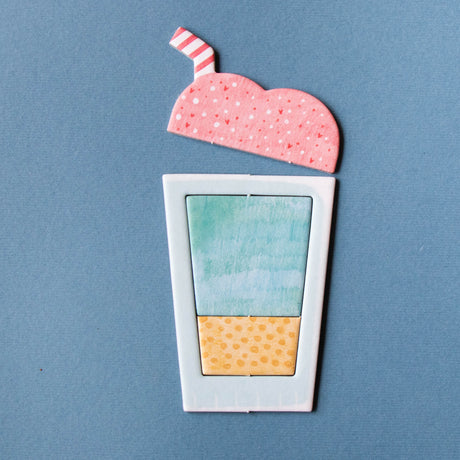 Toy milkshake puzzle piece with pink foam, striped straw, and blue and yellow liquid layers on a blue background.