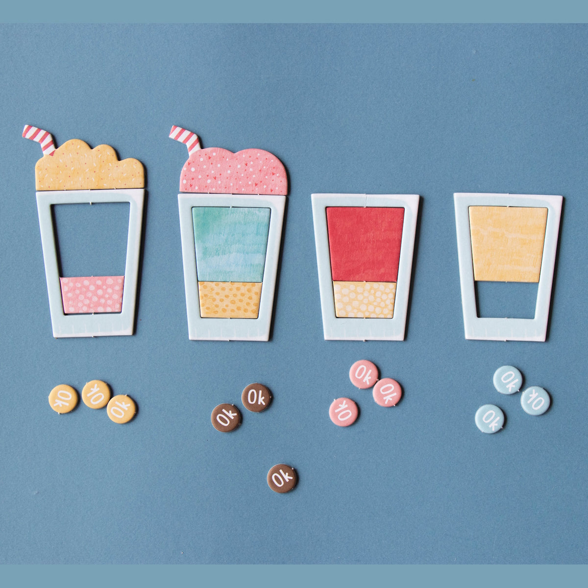 Colorful paper milkshake and drink cutouts with small round tokens on a blue background for a children's game.