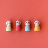 Four small, wooden rabbit peg dolls in green, red, blue, and yellow lined up against a solid red background.