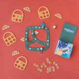 Londji Strawberries Tiny Game with green board, wooden tokens, and yellow baskets on a red background.