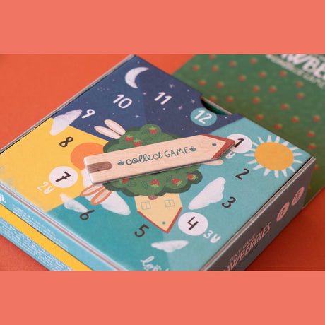 Londji Strawberries Tiny Game box with a wooden arrow spinner pointing to a clock face with sun and moon illustrations.