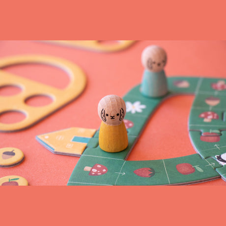 Londji wooden animal game pieces on a green forest-themed board game with strawberries, mushrooms, and acorns.