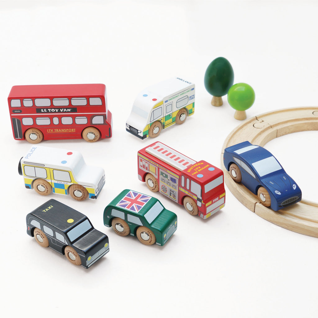 Toy wooden vehicles including a red double-decker bus, police car, ambulance, fire truck, green car, and black taxi. Playful and colorful.