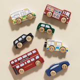 Top-down view of seven wooden London toy vehicles neatly arranged on a beige background.