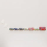 Seven wooden London toy vehicles in a line on a cream surface with paper clouds behind them.