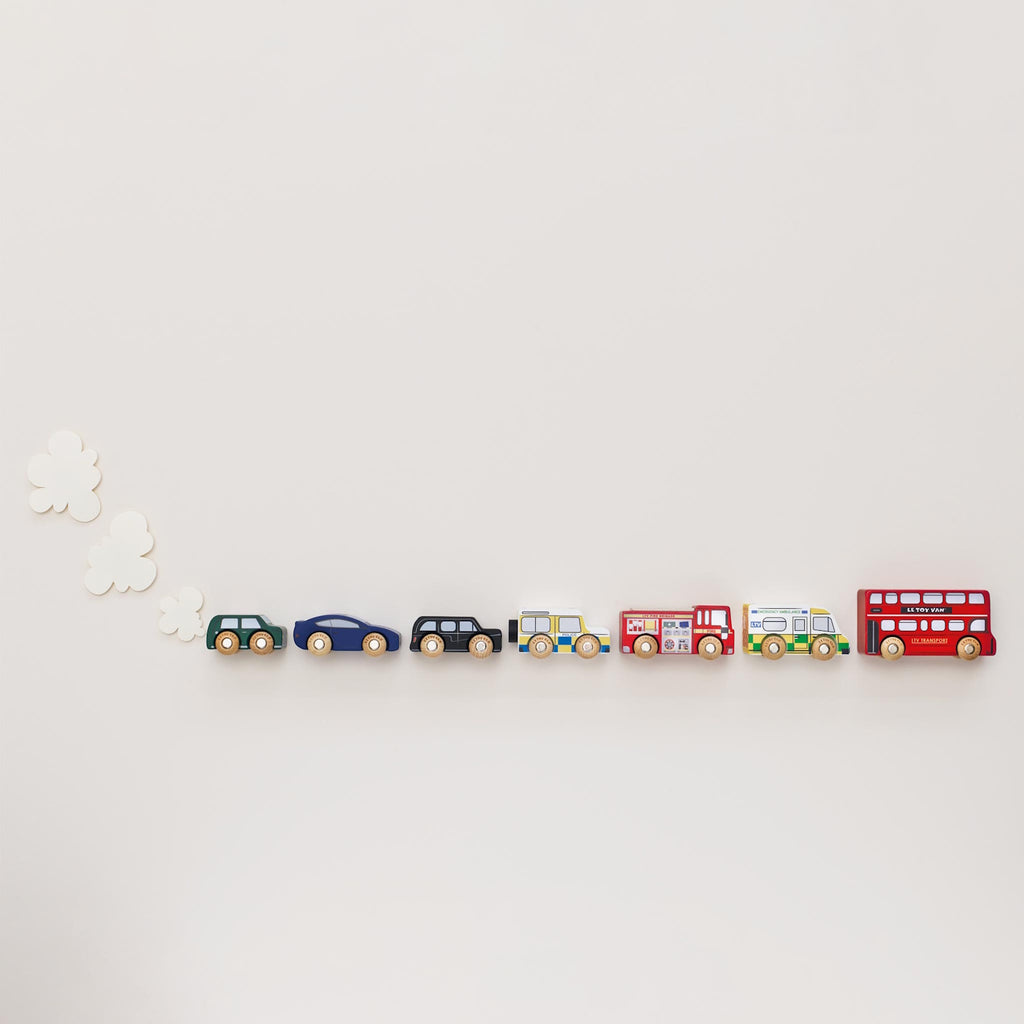 Toy wooden vehicles including a red double-decker bus, police car, ambulance, fire truck, green car, and black taxi. Playful and colorful.