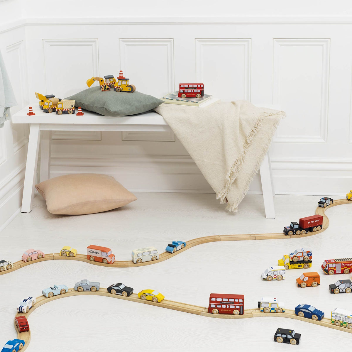 Wooden toy cars arranged on winding tracks across the floor in a bright playroom.