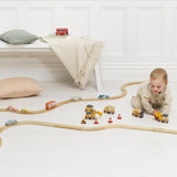 A toddler playing with wooden toy construction vehicles on a floor with wooden tracks.