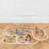 Wooden toy train set assembled on a herringbone wooden floor in front of a white wall.