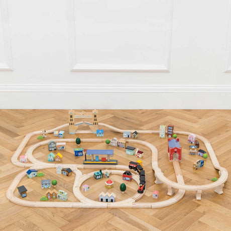 Wooden toy train set assembled on a herringbone wooden floor in front of a white wall.