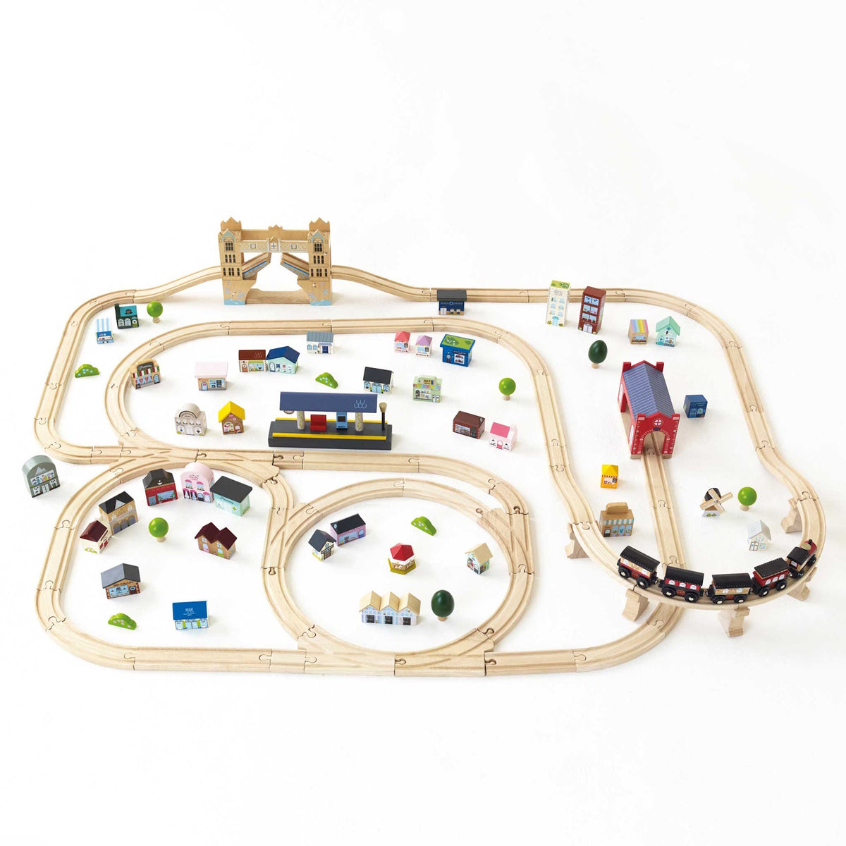 Wooden train set layout with miniature buildings, station, and bridge on a white surface.