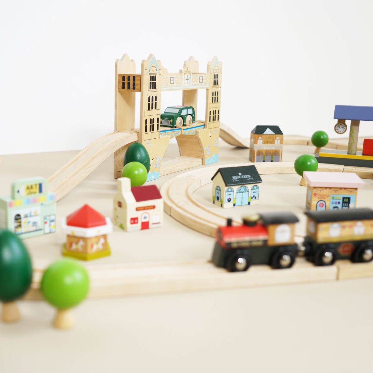 Wooden toy train on a track set with Tower Bridge, miniature shops, and trees in the background.