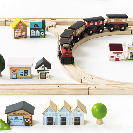 Wooden toy train on a curved track, surrounded by mini shops and houses on a white surface.