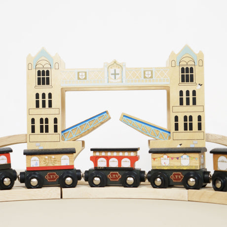 Wooden toy train carriages on a track in front of an open Tower Bridge feature.