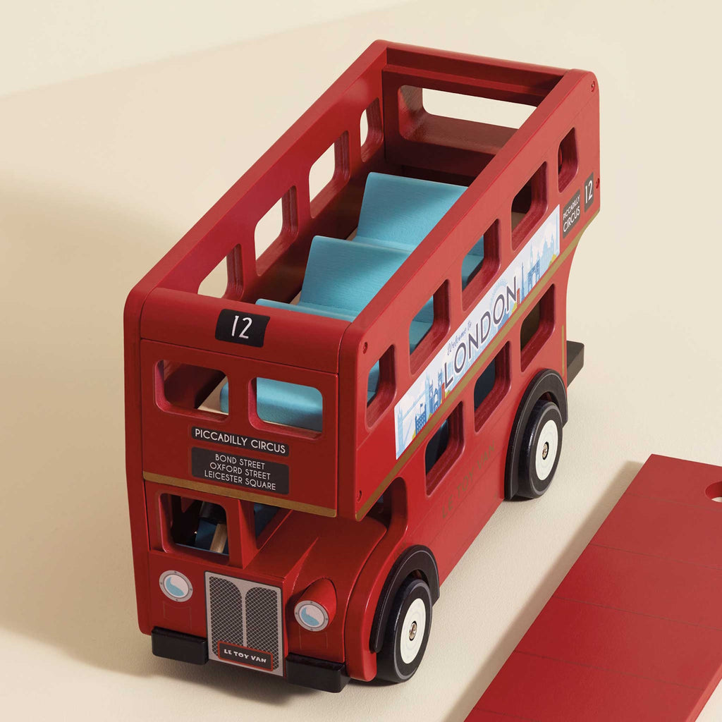 Toy red double-decker bus with a "Welcome to London" sign, featuring a wooden driver figure.