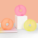 Three colorful ring-shaped gel stress toys displayed on grid pedestal and pastel notebooks.