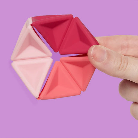 A hand holding a pink silicone hexaflexagon fidget toy against a light purple background.