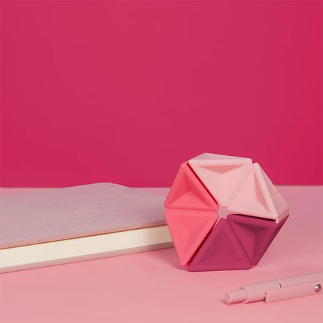 Pink silicone hexaflexagon fidget toy upright on a desk next to a book and pen.