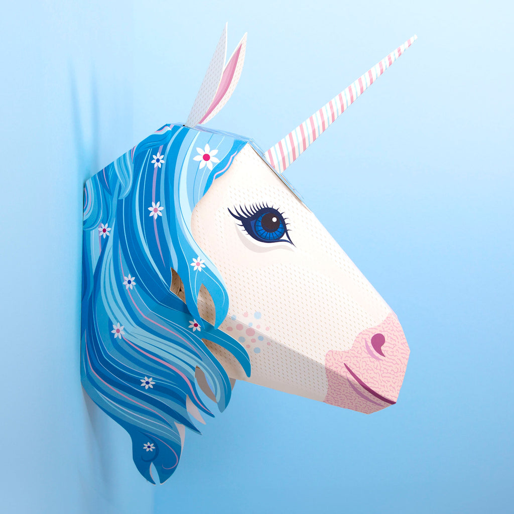 A whimsical 3D unicorn head with a pink-striped horn and flowing blue mane adorned with flowers, set against a pastel blue background.