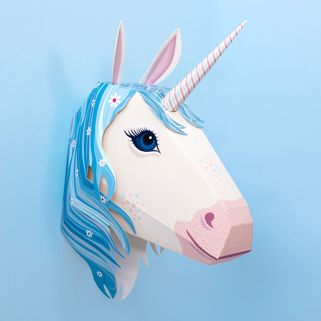 A whimsical 3D unicorn head with a pink-striped horn and flowing blue mane adorned with flowers, set against a pastel blue background.